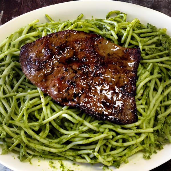 Grilled steak with a glossy glaze served over a bed of green pesto pasta.