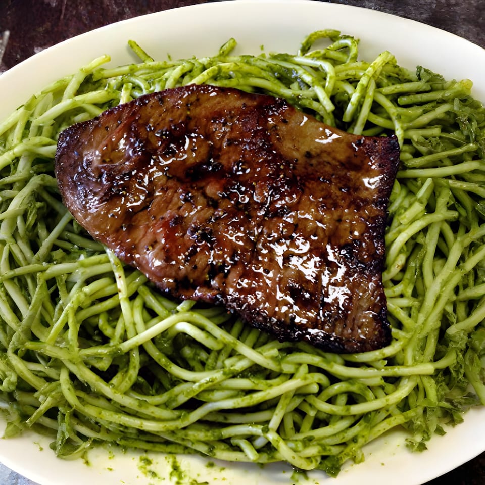 Grilled steak with a glossy glaze served over a bed of green pesto pasta.