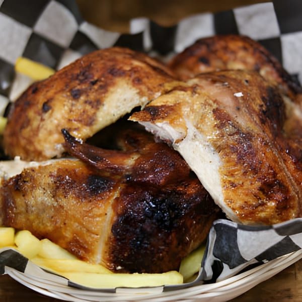 Golden brown roasted chicken pieces and french fries in a checkered paper-lined basket.